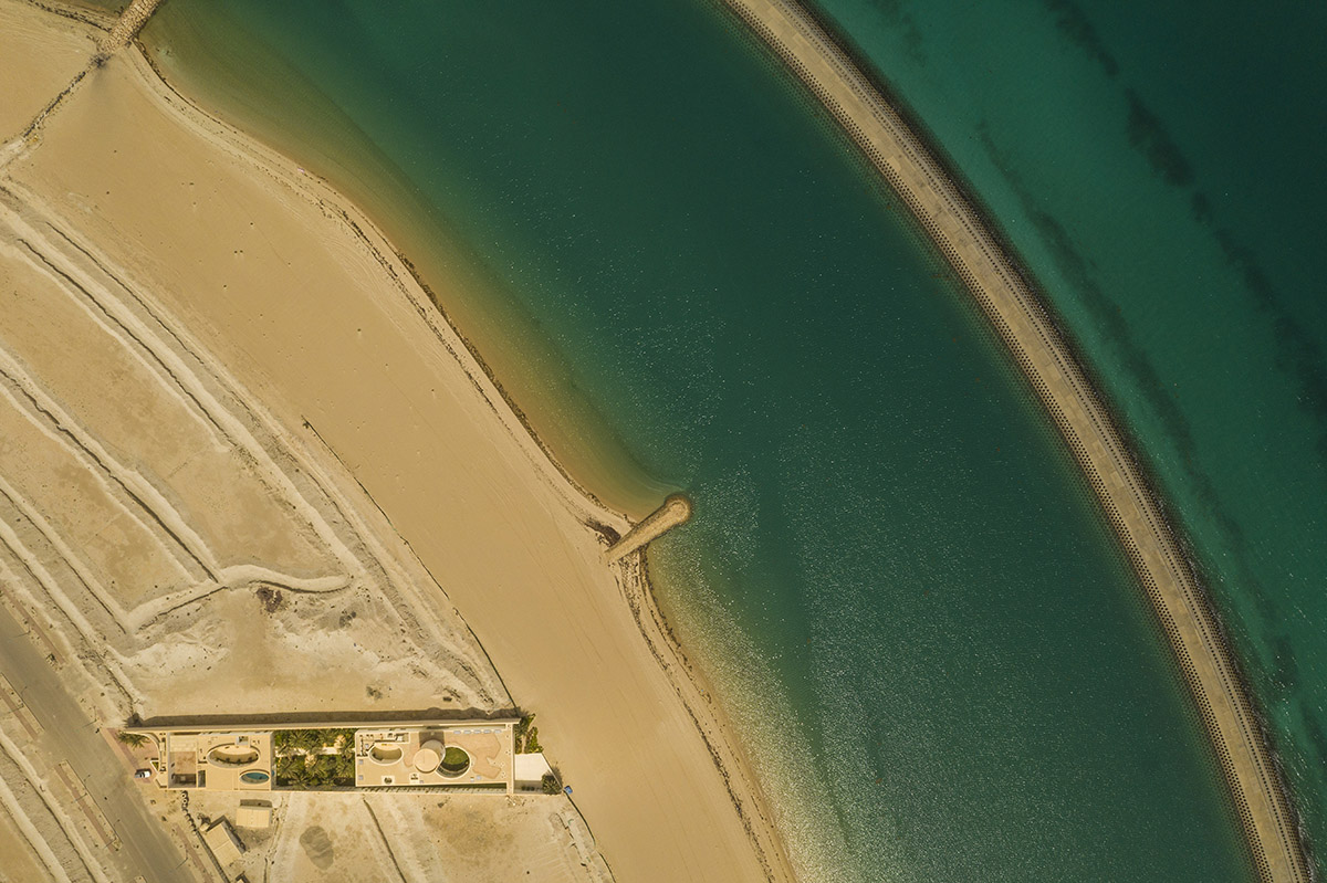 White Fortress by TAEP/AAP is a linear house that features a tall cylindrical lighthouse on a beach 