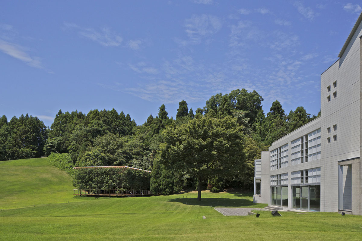 A multi-purpose venue is wrapped by living trees as an addition to open-air theatre in Japan
