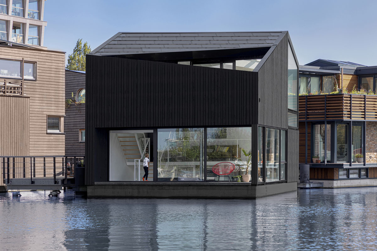 i29 built floating house with black timber and cut-out roof as part of floating village in Amsterdam
