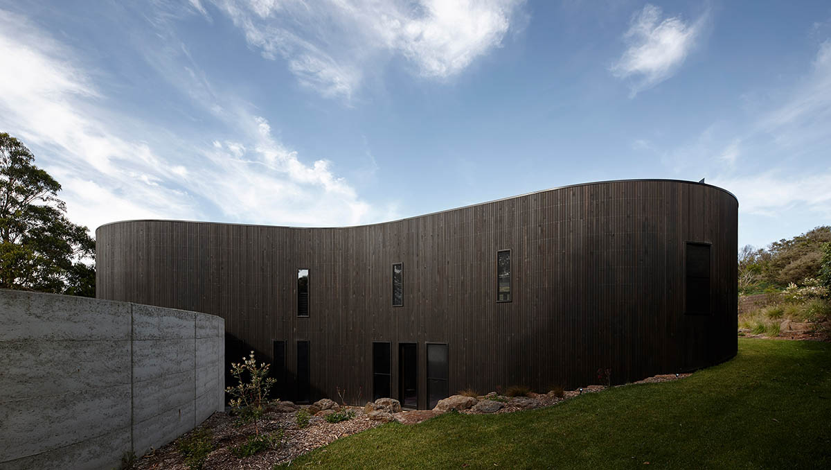 Wood Marsh built curvaceous home clad in dark timber contrasting its natural landscape in Portsea