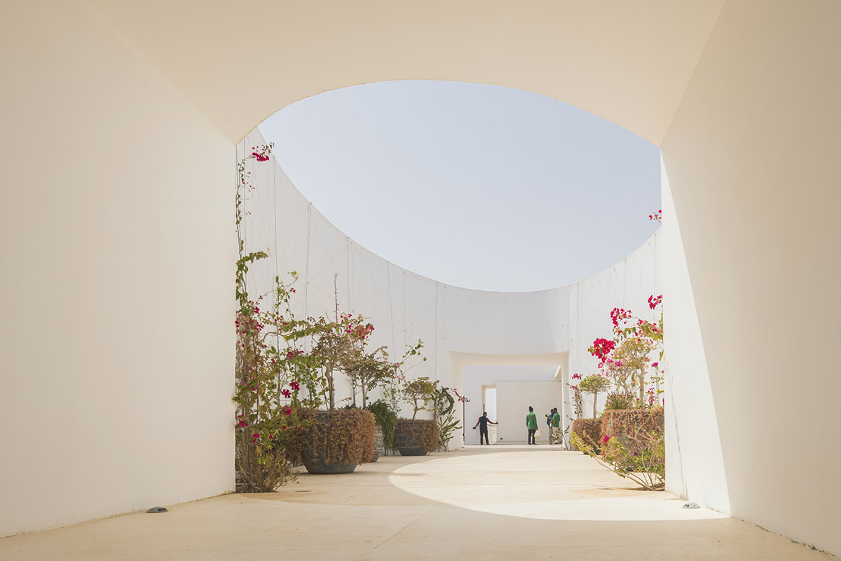 White Fortress by TAEP/AAP is a linear house that features a tall cylindrical lighthouse on a beach 