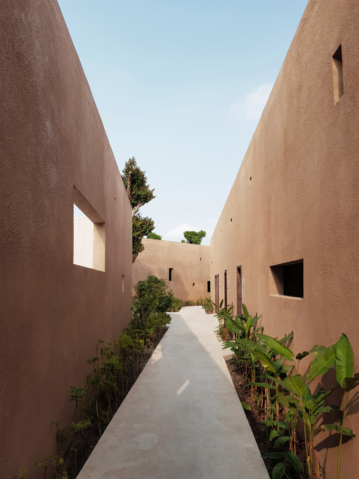 TAA DESIGN built public space with pitched roofs and rough concrete walls painted with pink tones