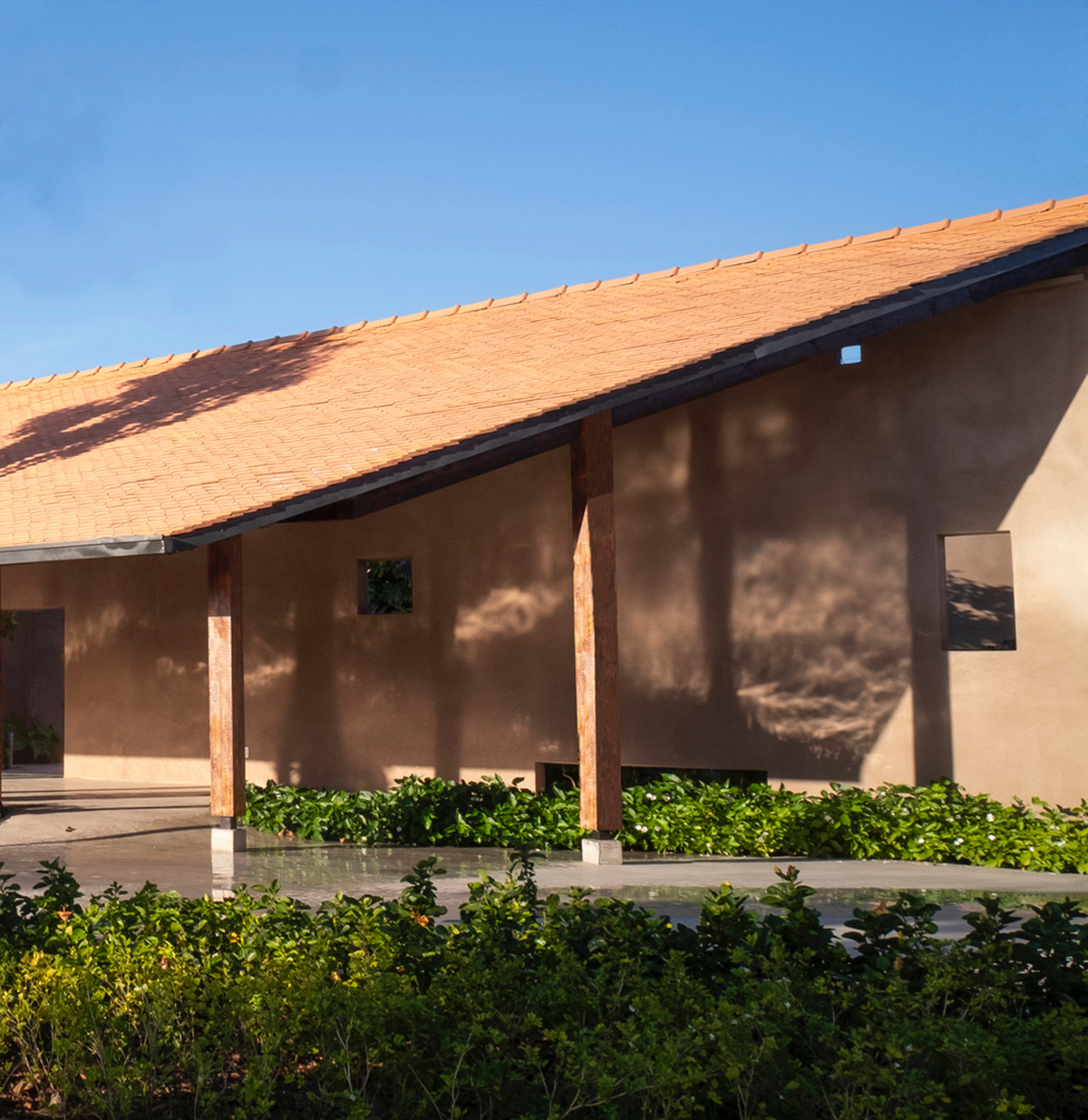 TAA DESIGN built public space with pitched roofs and rough concrete walls painted with pink tones