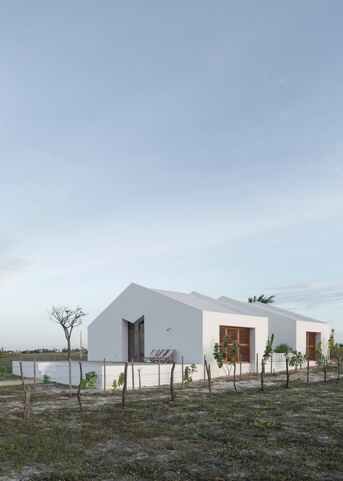 Two identical all-white volumes form this house by Atelier Branco Arquitetura on a flat landscape