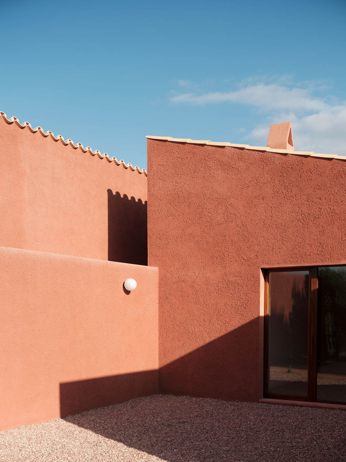 Large openings and reddish-colored façades mark this holiday home by Isla Architects in a rustic land