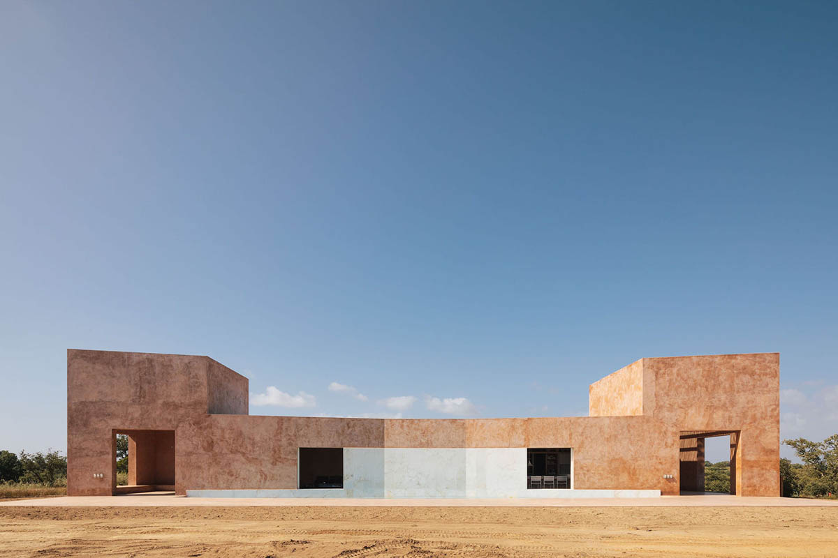 Castle-like red-pigmented house features recessed volumes on arid landscape of Alentejo