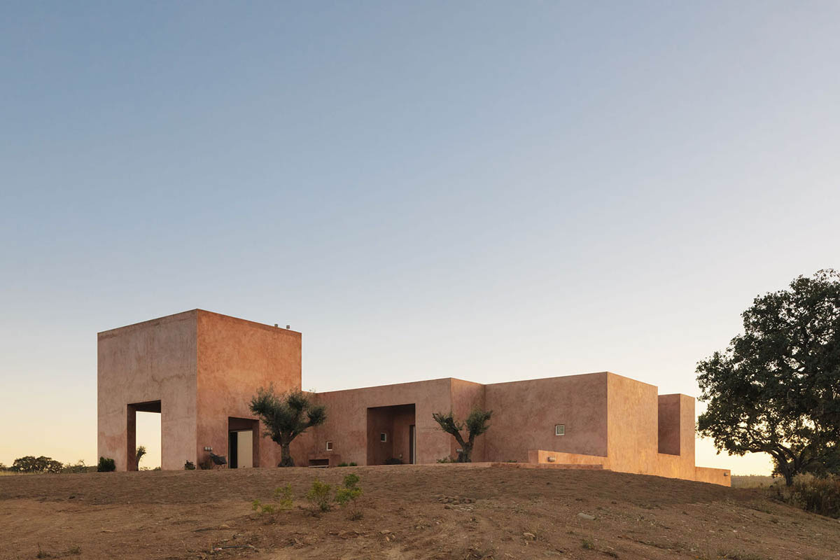 Castle-like red-pigmented house features recessed volumes on arid landscape of Alentejo