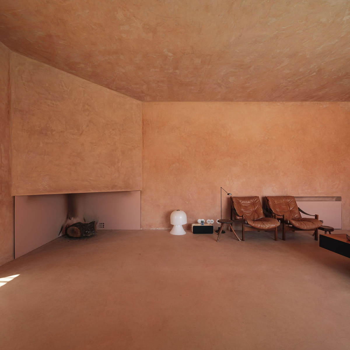 Castle-like red-pigmented house features recessed volumes on arid landscape of Alentejo