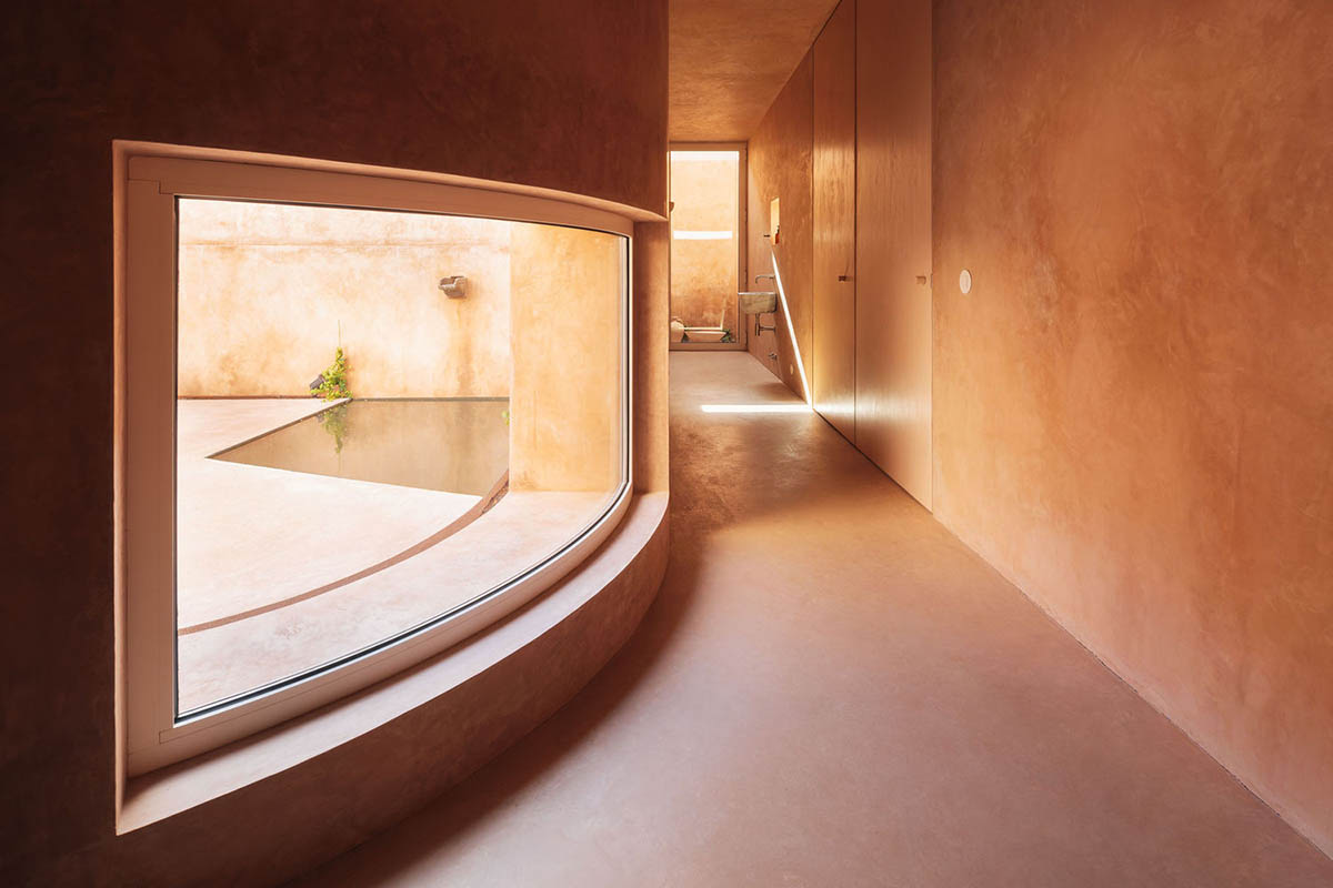 Castle-like red-pigmented house features recessed volumes on arid landscape of Alentejo