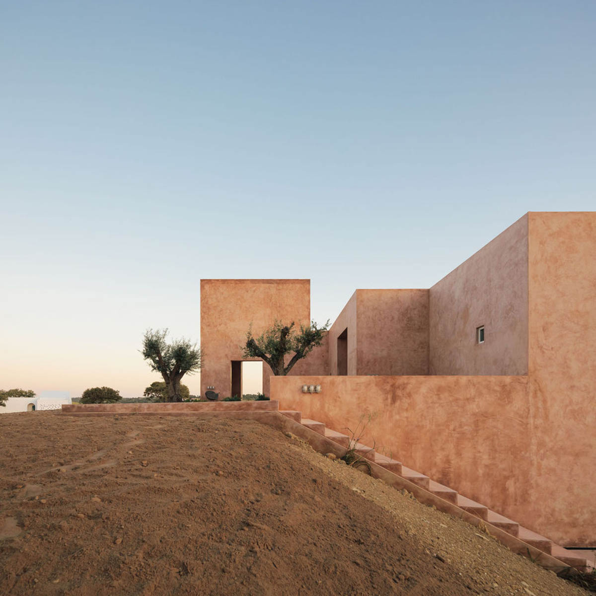 Castle-like red-pigmented house features recessed volumes on arid landscape of Alentejo