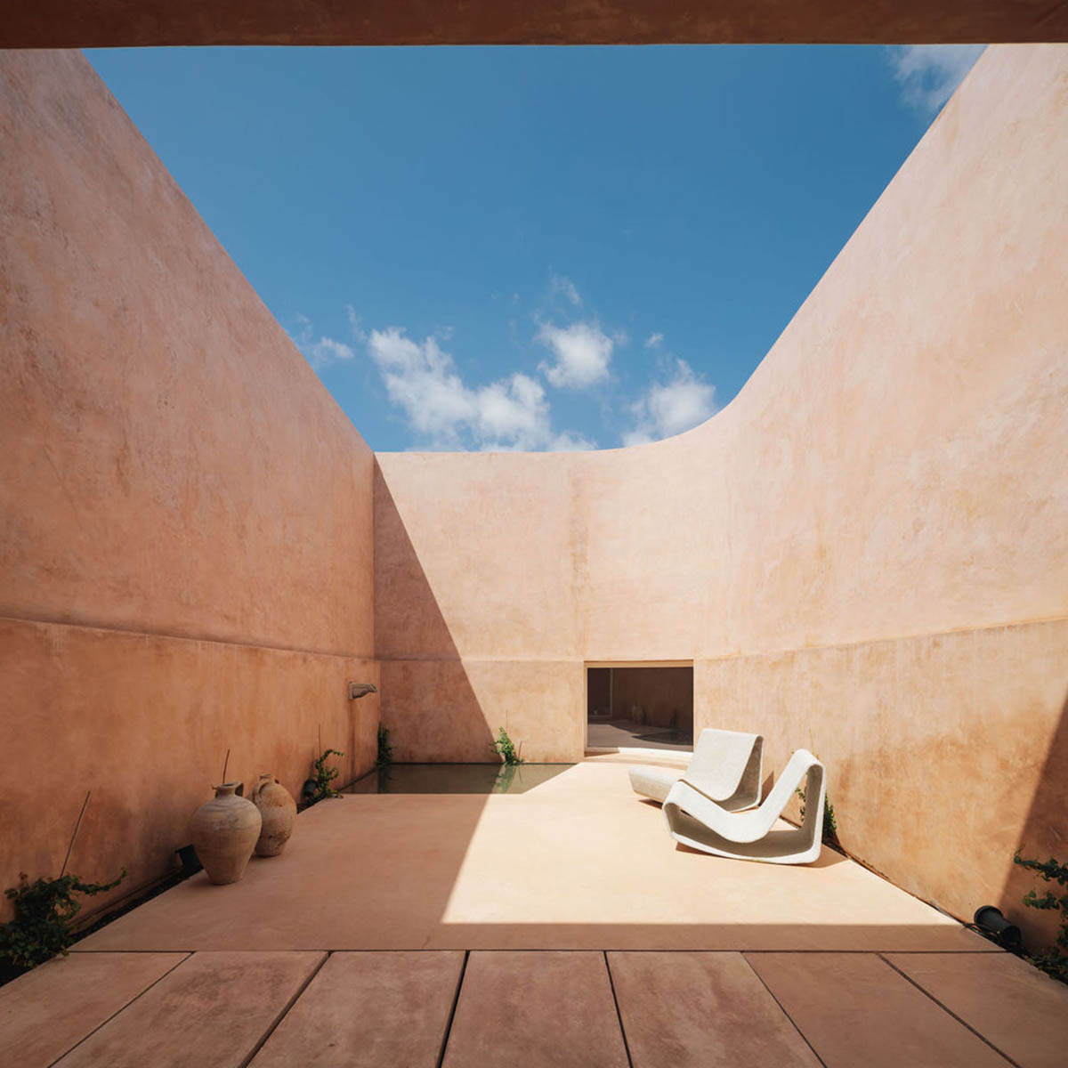 Castle-like red-pigmented house features recessed volumes on arid landscape of Alentejo