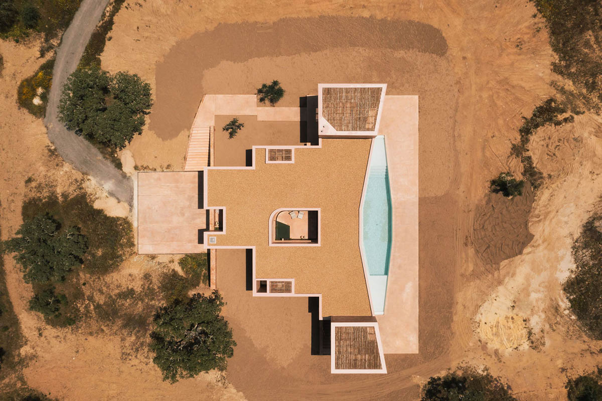 Castle-like red-pigmented house features recessed volumes on arid landscape of Alentejo