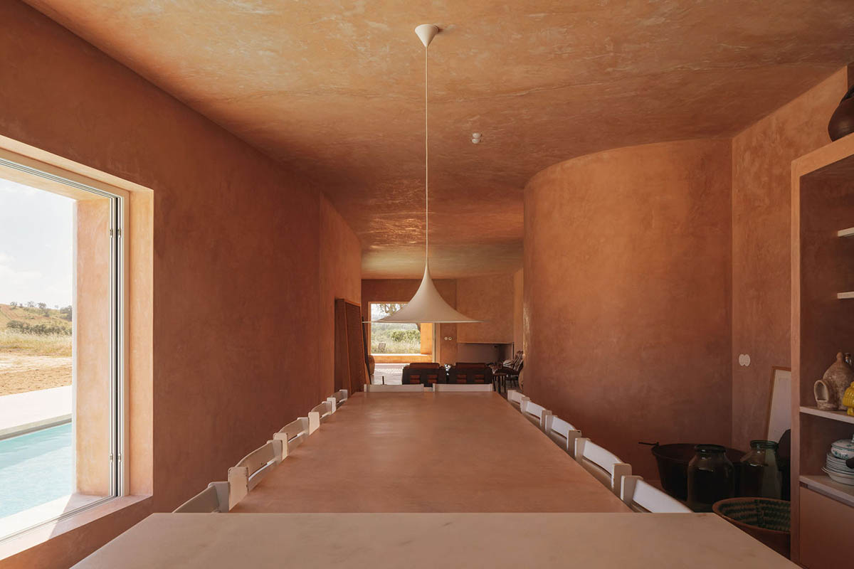 Castle-like red-pigmented house features recessed volumes on arid landscape of Alentejo