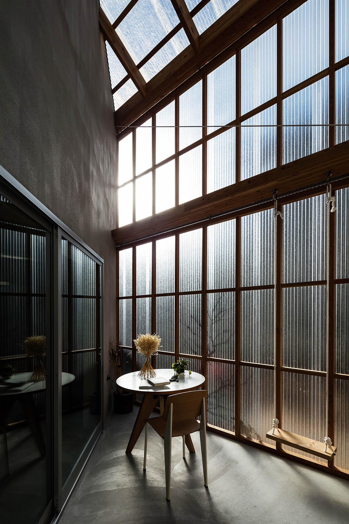 Huge corrugated polycarbonate wall lightens a cornered sunroom in house by Tato Architects