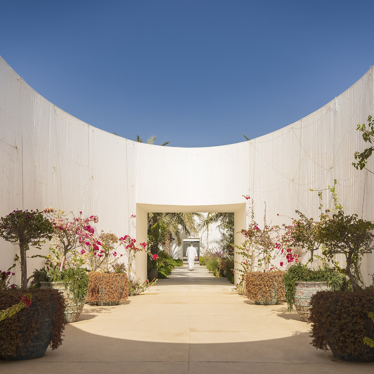 White Fortress by TAEP/AAP is a linear house that features a tall cylindrical lighthouse on a beach 