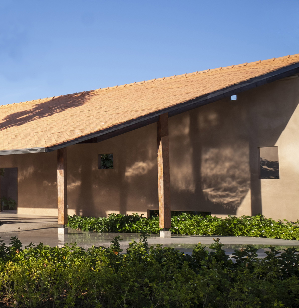 TAA DESIGN built public space with pitched roofs and rough concrete walls painted with pink tones