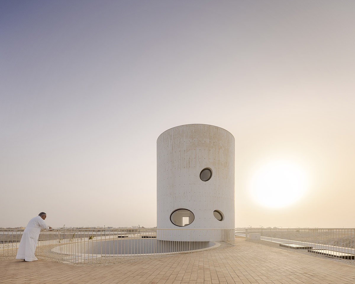 White Fortress by TAEP/AAP is a linear house that features a tall cylindrical lighthouse on a beach 