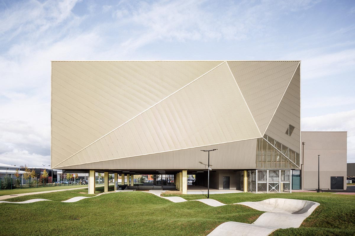 The gold-colored, folded facade gives a striking and symbolic presence to a new sports complex 