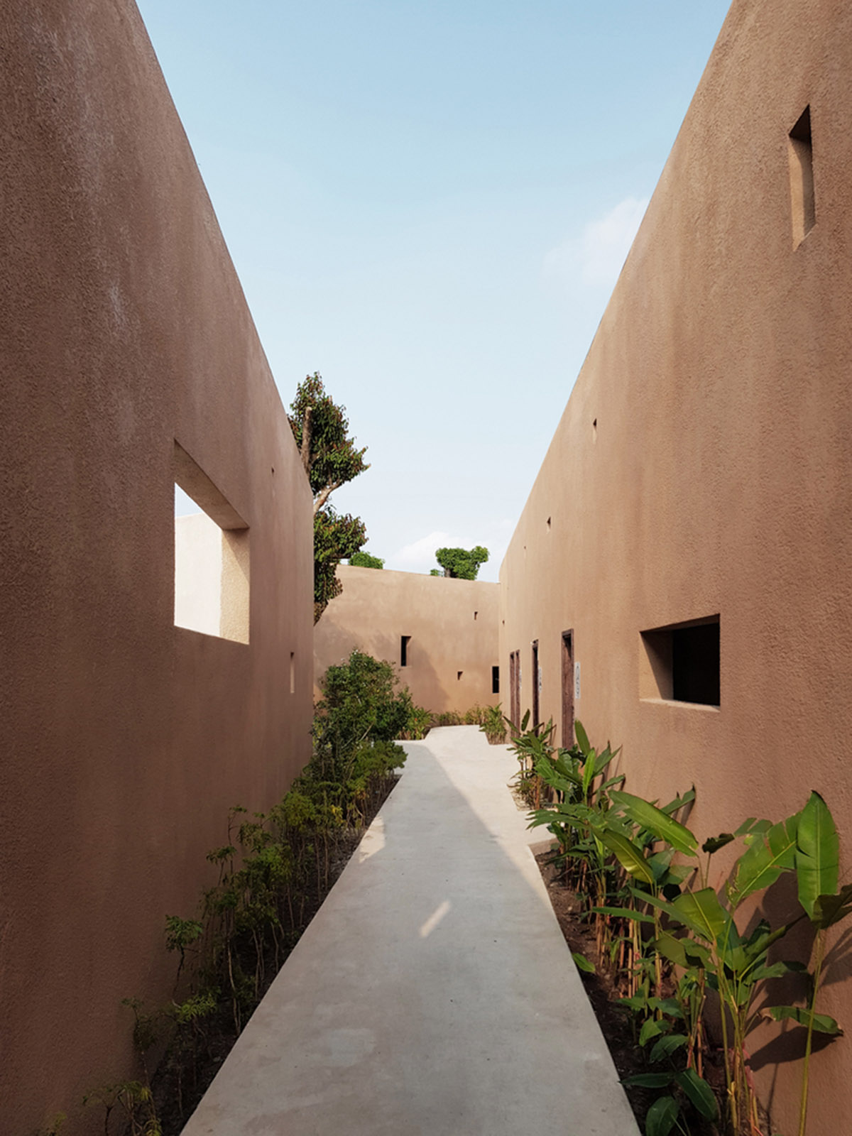 TAA DESIGN built public space with pitched roofs and rough concrete walls painted with pink tones