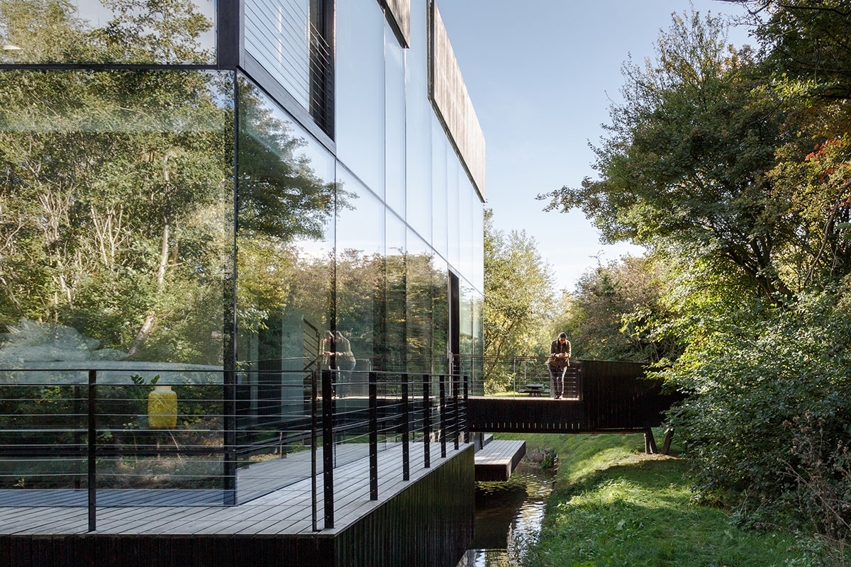 Mecanoo completes glass villa with dark stripes on a lake in Lechlade
