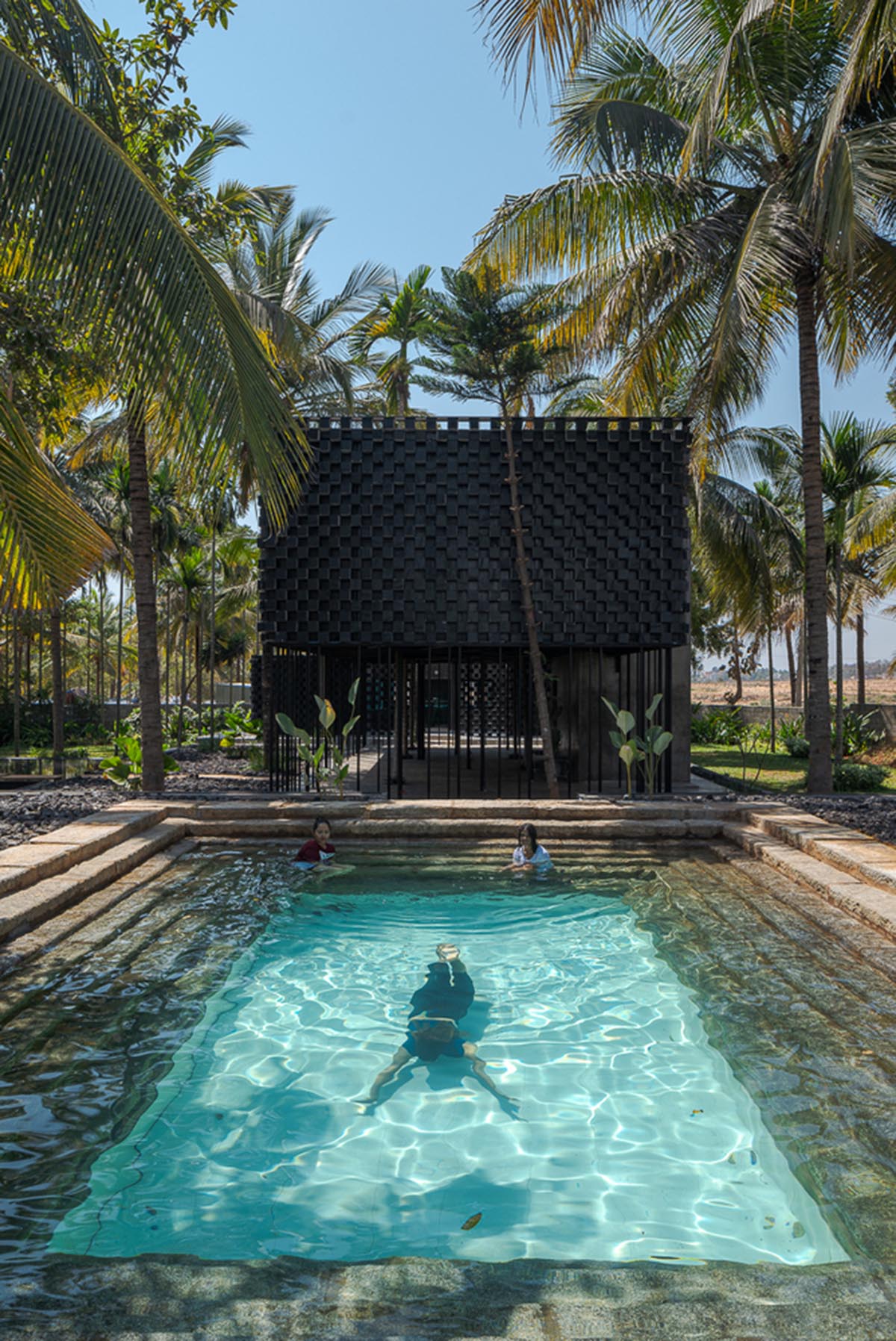Parallax designs black weekend house raised on slender stilts within coconut trees in Bangalore