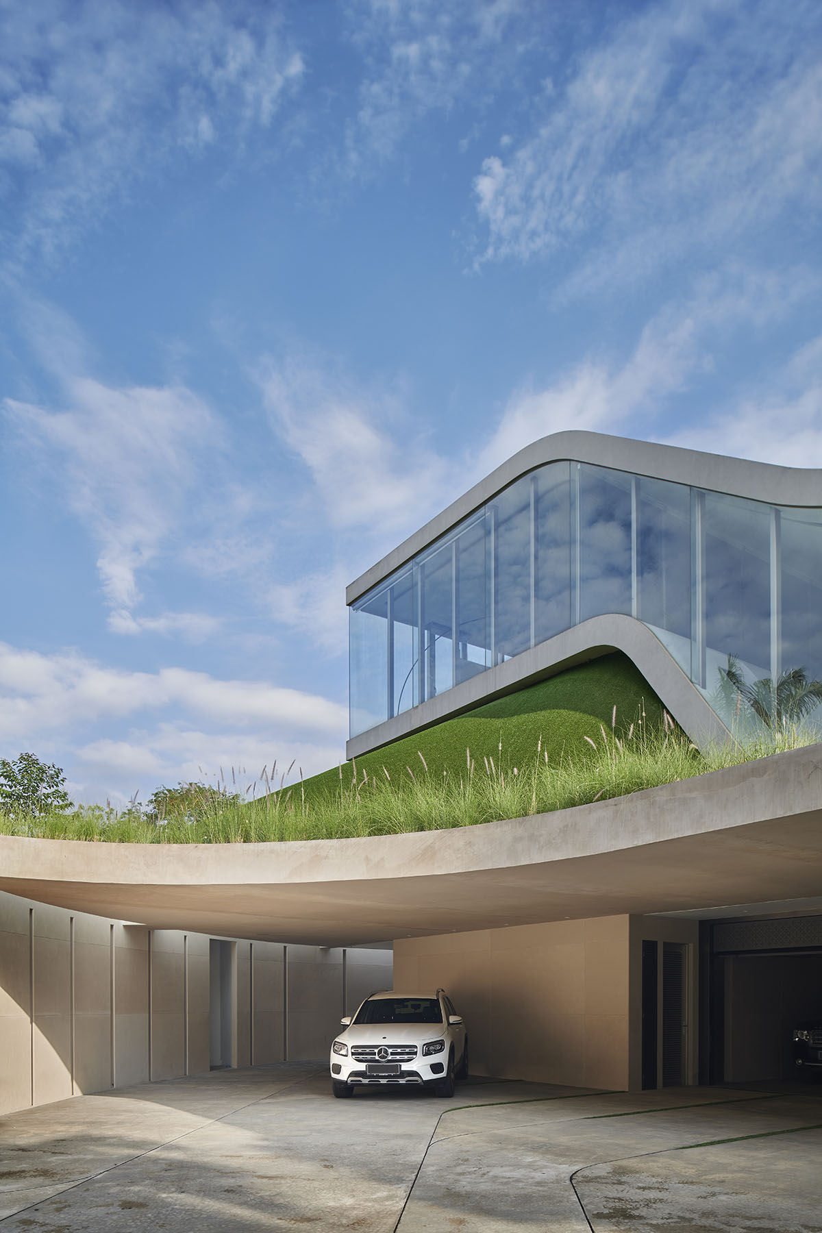 Undulating residence by RDMA is placed onto grass covered earth mound in Indonesia