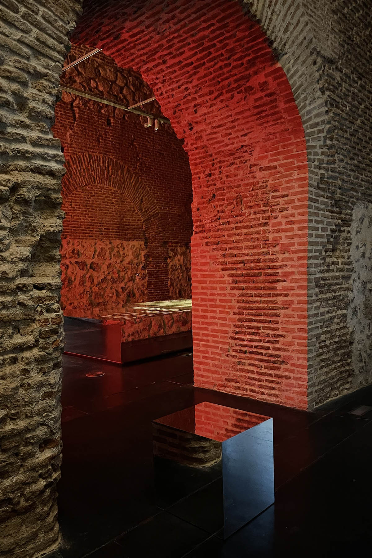 Exhibition design at Condeduque Center’s vaulted hall plays with red light, mirrors and reflections