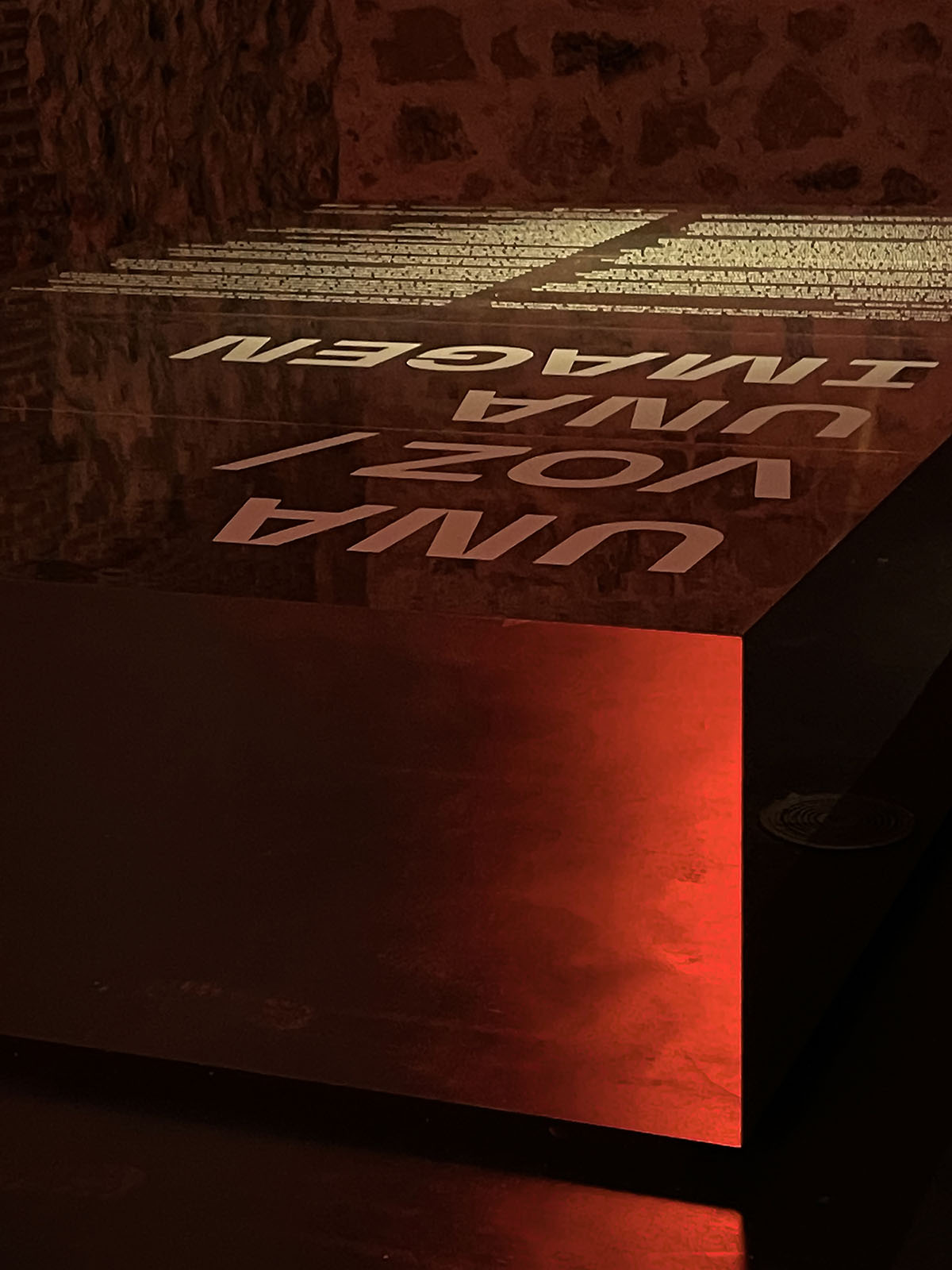 Exhibition design at Condeduque Center’s vaulted hall plays with red light, mirrors and reflections