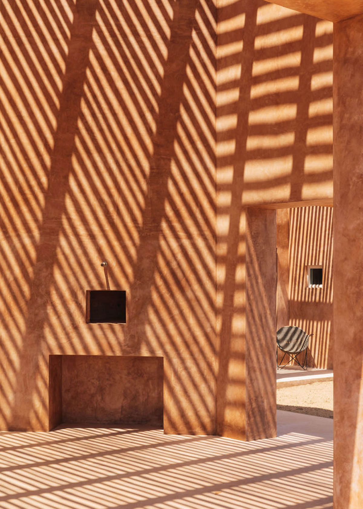 Castle-like red-pigmented house features recessed volumes on arid landscape of Alentejo