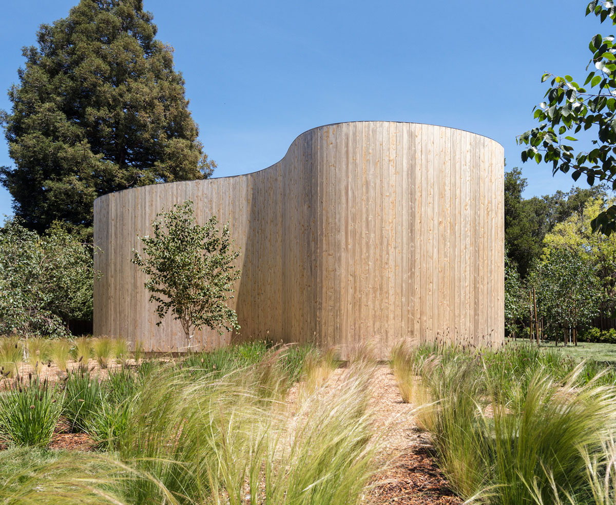 Curving wooden walls form Roofless House among trees in Atherton
